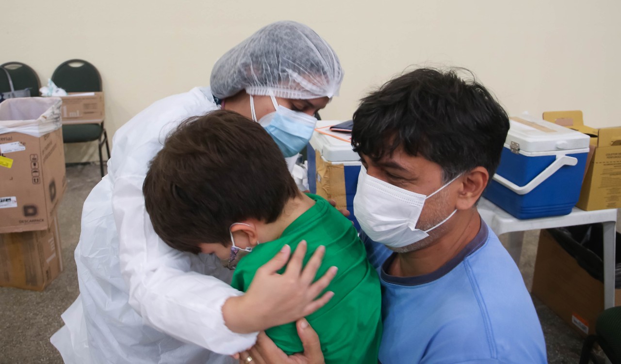 enfermeira vacinando uma criança que está no colo do pai
